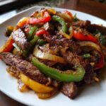 A close-up of perfectly cooked steak fajita strips mixed with sautéed red, green, and yellow bell peppers and onions.