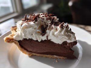 A decadent slice of french silk pie featuring a thick chocolate filling, topped with whipped cream and chocolate shavings.