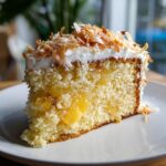 Close-up of a moist slice of hawaiian wedding cake filled with pineapple and topped with white frosting and toasted coconut flakes.
