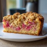 Close-up of a moist slice of spring rhubarb cake with almond topping, showing bright pink rhubarb chunks.