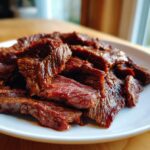 Close-up of thinly sliced, deep red steak pieces coated in a rich fajita marinade, served on a white plate.