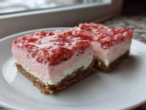Two squares of strawberry crunch cheesecake bars showing graham cracker crust, cream cheese layer, and strawberry topping.