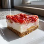 Close-up of a square slice of strawberry crunch cheesecake with a graham cracker crust.