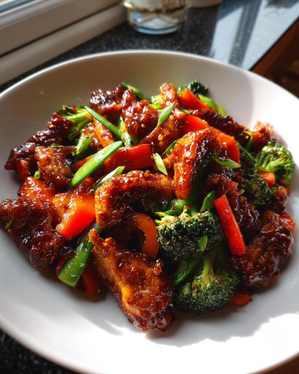 Close-up of glossy teriyaki chicken stir fry mixed with bright green broccoli florets and red bell pepper strips.