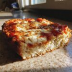 Close-up of a thick slice of pizza made with cottage cheese pizza crust, topped with melted mozzarella and herbs.