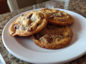 Three golden brown classic chocolate chip cookies with melted chunks of chocolate served on a white plate.