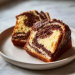 Two thick slices of moist german marble cake showing distinct vanilla and chocolate swirls on a light plate.