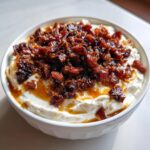 Close-up of a bowl of whipped feta dip topped generously with caramelized bacon and dates.