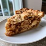 A generous slice of Classic Homemade Apple Pie showing thick, spiced apple filling and a golden, flaky, sugared crust.