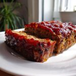 Two thick slices of Classic Homemade Meatloaf topped with a shiny, thick red glaze, served on a white plate.