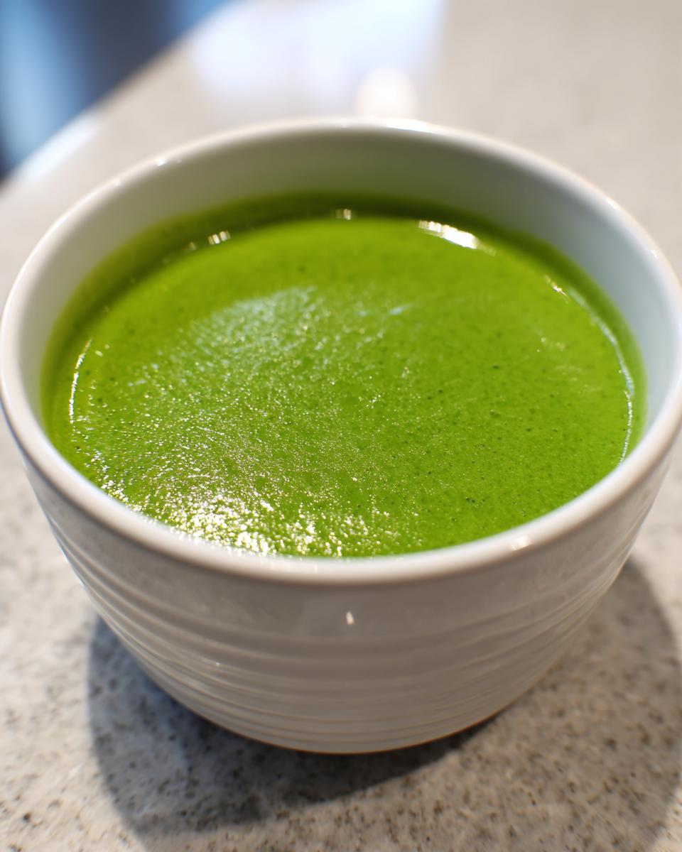Close-up of a white bowl filled with bright green, creamy asparagus soup.