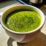 Close-up of vibrant green Creamy Asparagus Soup with frothy top served in a white mug.