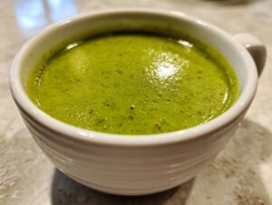 A close-up of vibrant green, creamy asparagus soup served in a white, ribbed mug or bowl.