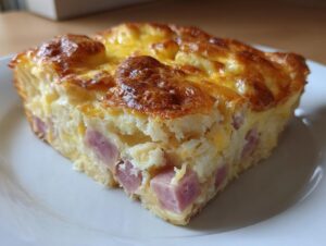 Close-up of a golden-brown slice of Make Ahead Ham and Swiss Brunch Bake on a white plate.