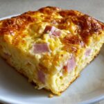 Close-up of a golden-brown slice of Make Ahead Ham and Swiss Brunch Bake showing chunks of ham in a fluffy egg and cheese base.