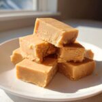 A stack of creamy, square pieces of Old Fashioned Peanut Butter Fudge piled on a white plate.