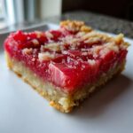 A close-up, appetizing shot of a single square of Rhubarb Dream Bars showing the thick, bright red rhubarb filling and crumbly crust.