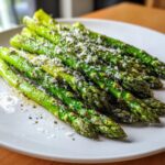 A close-up of bright green Roasted Asparagus with Lemon and Parmesan served on a white plate.