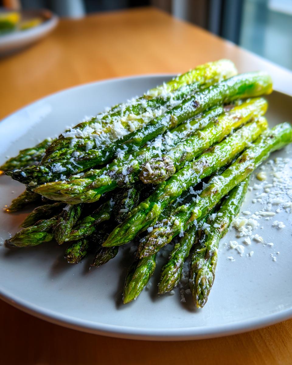 A pile of bright green Roasted Asparagus with Lemon and Parmesan served on a light gray plate.