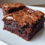 A close-up shot highlighting the rich, dark interior and crackly top of Seriously Fudgy Homemade Brownies served on a white plate.