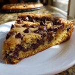 A thick, gooey slice of Chocolate Chip Cookie Cake loaded with melted chocolate chips, served on a white plate.