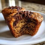 A close-up of a Sourdough Discard Chocolate Chip Muffin with a bite taken out, showing melted chocolate chips on top.