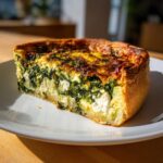 A thick slice of baked Spinach and Feta Quiche showing a rich filling of green spinach and white feta cheese.