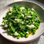 Close-up of a bright Spring Pea and Feta Salad topped with fresh mint leaves and olive oil.