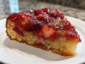 A close-up of a moist slice of Strawberry Rhubarb Upside Down Cake with a glossy, caramelized strawberry topping.